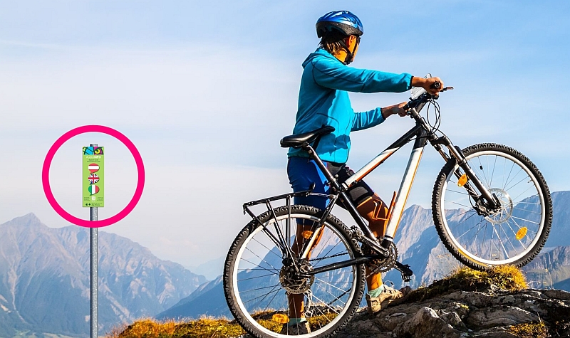 Mann mit Mountainbike auf Berggipfel genießt Panorama. Daneben ein Schild mit Audio Info über einen NFC Speech Tag