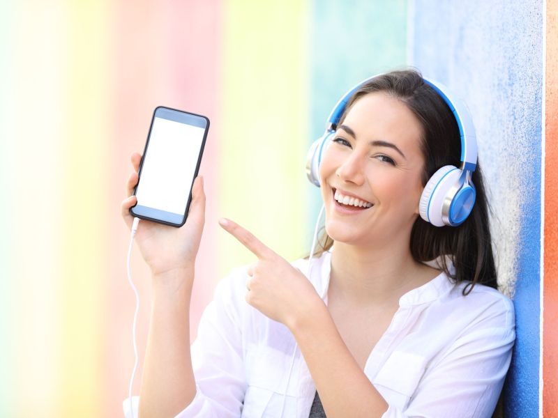 Happy girl listening is showing smart phone screen in a colorful street