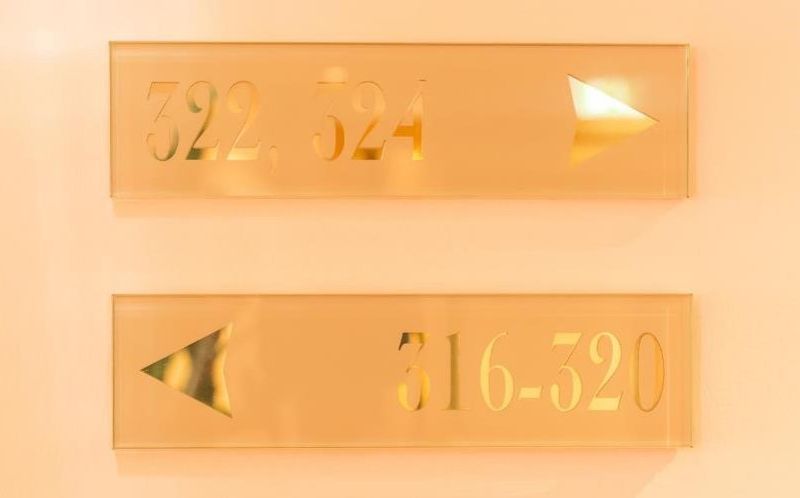 Two transparent plastic signs on a golden yellow wall. On them, made of shiny gold paint, room numbers. Not accessible signs