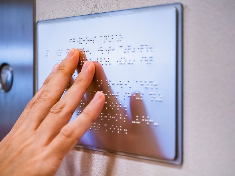 Hand liest Brailleschrift auf Wandschild aus Metall