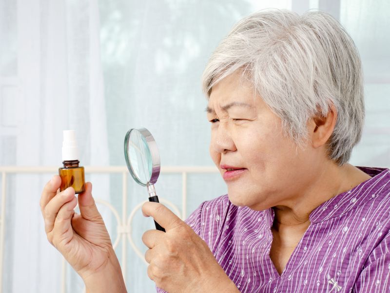 Elderly woman with a magnifying glass, who is trying to read the label on a small medicine bottle