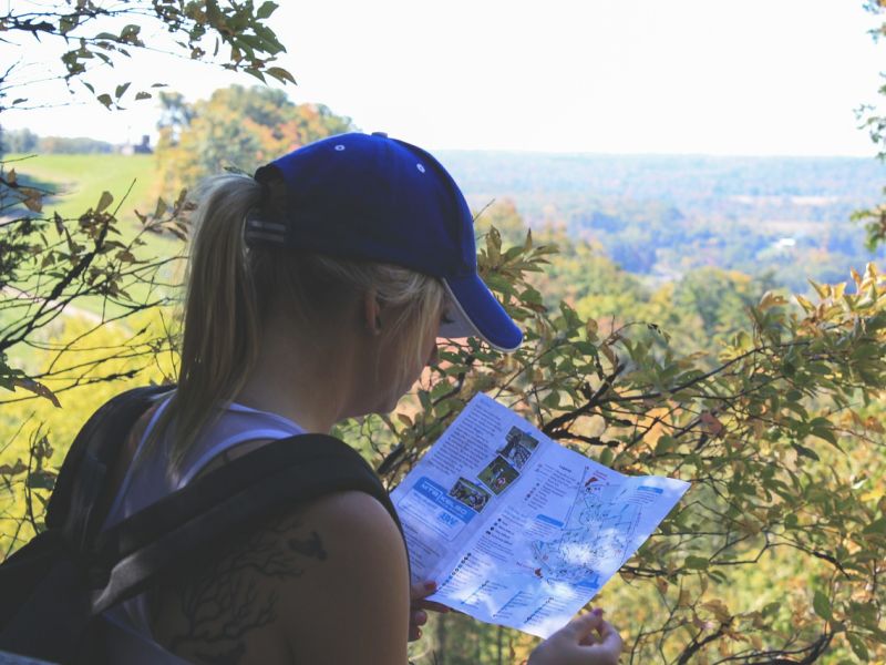 Young woman with cap and backback checks her paper hiking guide 