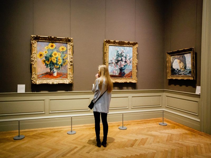 Blonde woman in a museum, standing in front of paintings behind a distancing bar