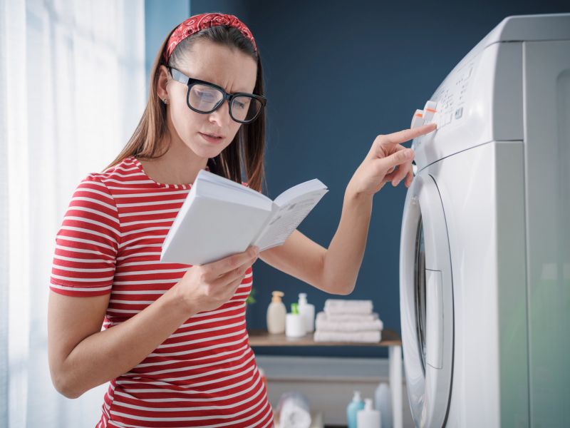 Frau liest Handbuch vor Waschmaschine mit Hand auf den Bedienelementen - hörbare handbücher würden helfen