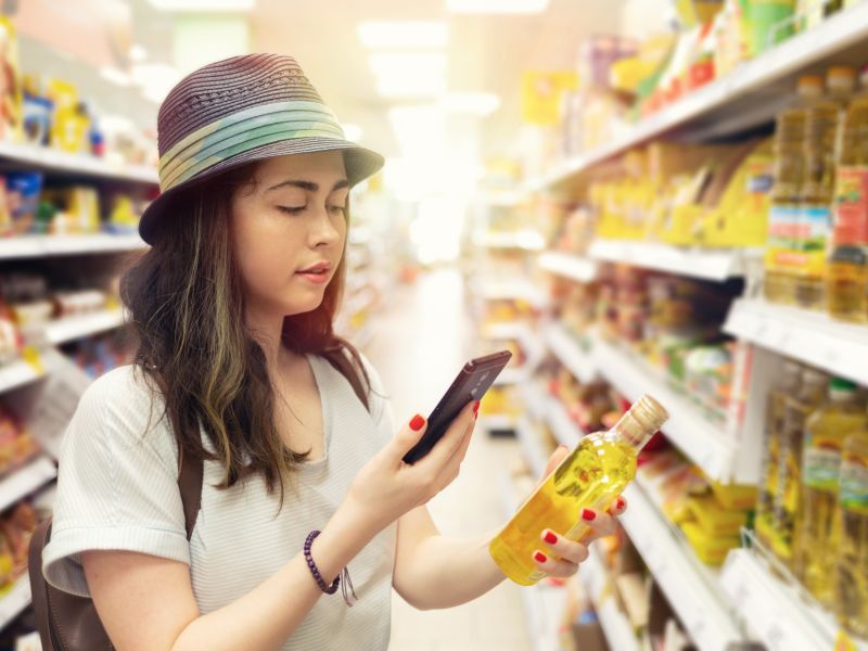 Young woman listens to audio QR Code on an oil bottle in the supermarket.